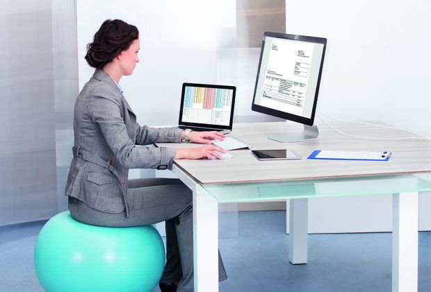 Frau sitzt auf Hüpfball am Schreibtisch Frau sitzt auf Hüpfball am Schreibtisch