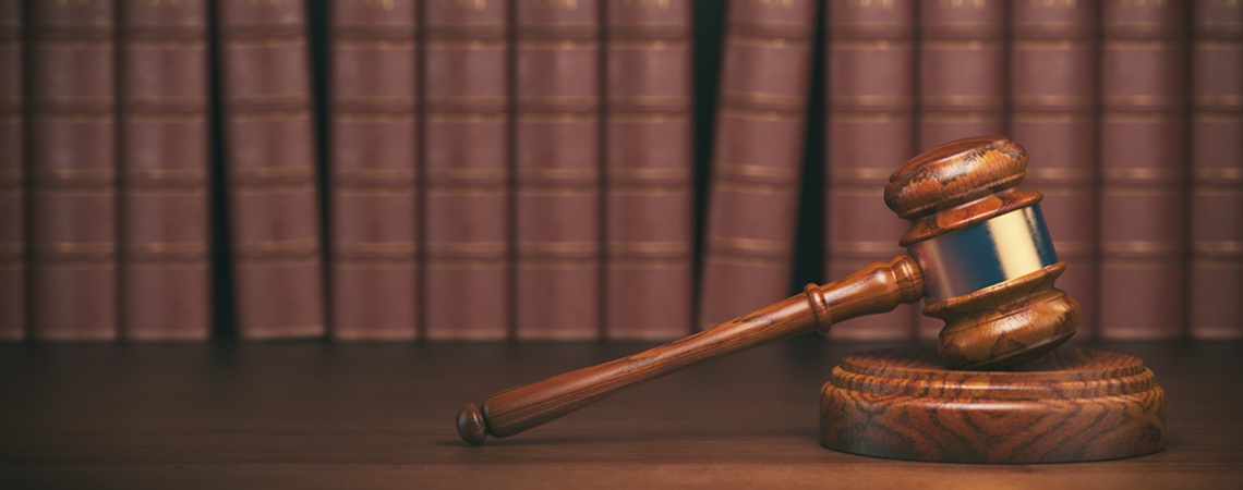ein Gerichtshammer mit Gesetzesbüchern im Hintergrund